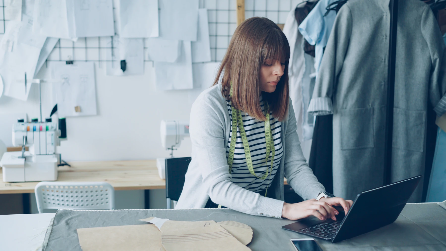 Fashion designer using a laptop among fabric and tools in her atelier
