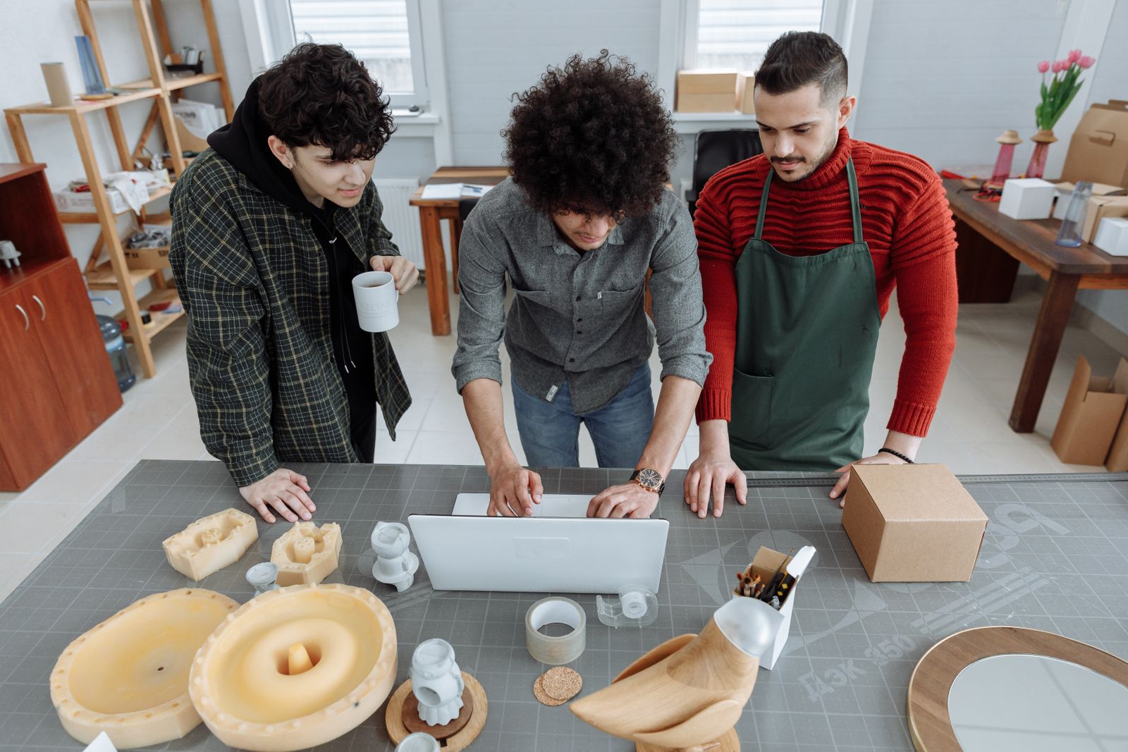 Three small-business team members reviewing work around a laptop in a bright workshop